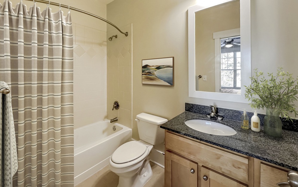 Bathroom with shower/bathtub combo, black countertops, wood cabinets, a toilet, and mirror at The Townhomes at Chapel Watch Village