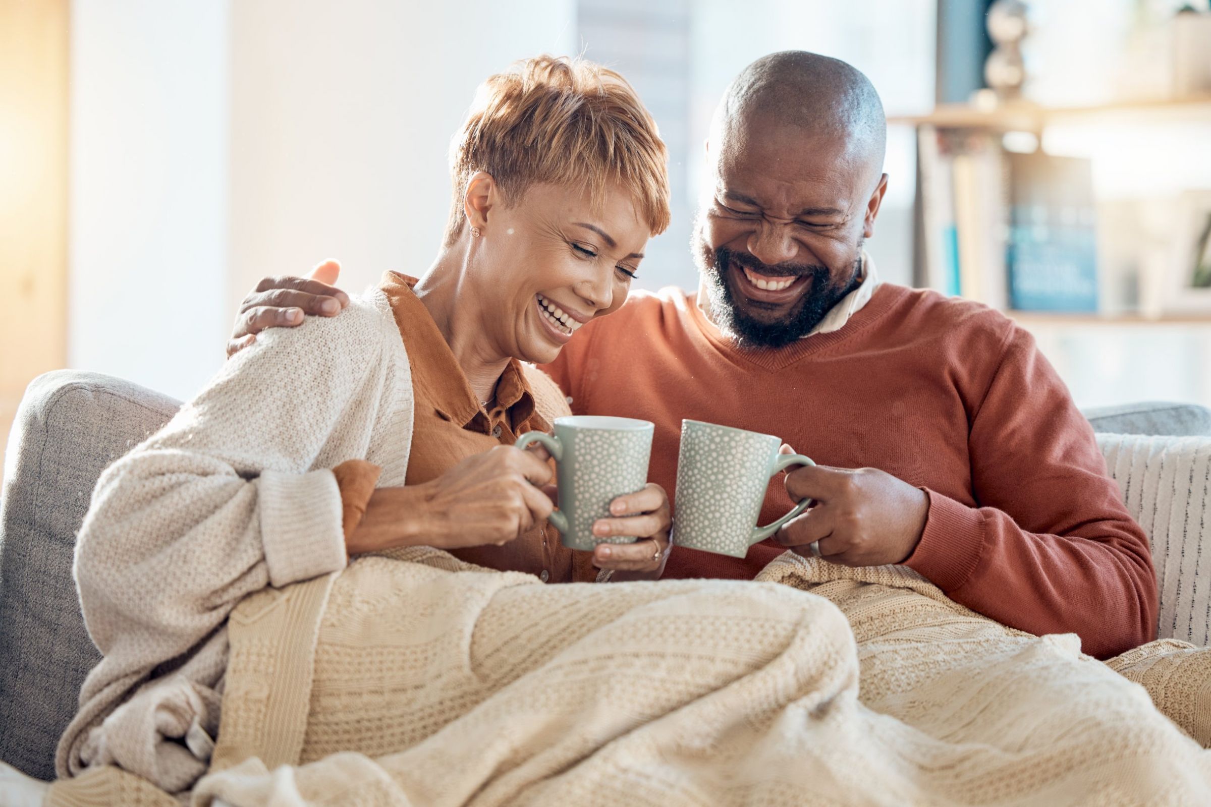 The Townhomes at Chapel Watch Village in Chapel Hill, NC with a middle aged couple drinking coffee on the couch with a blanket and laughing